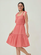Woman wearing a coral dress with bow straps on a plain background