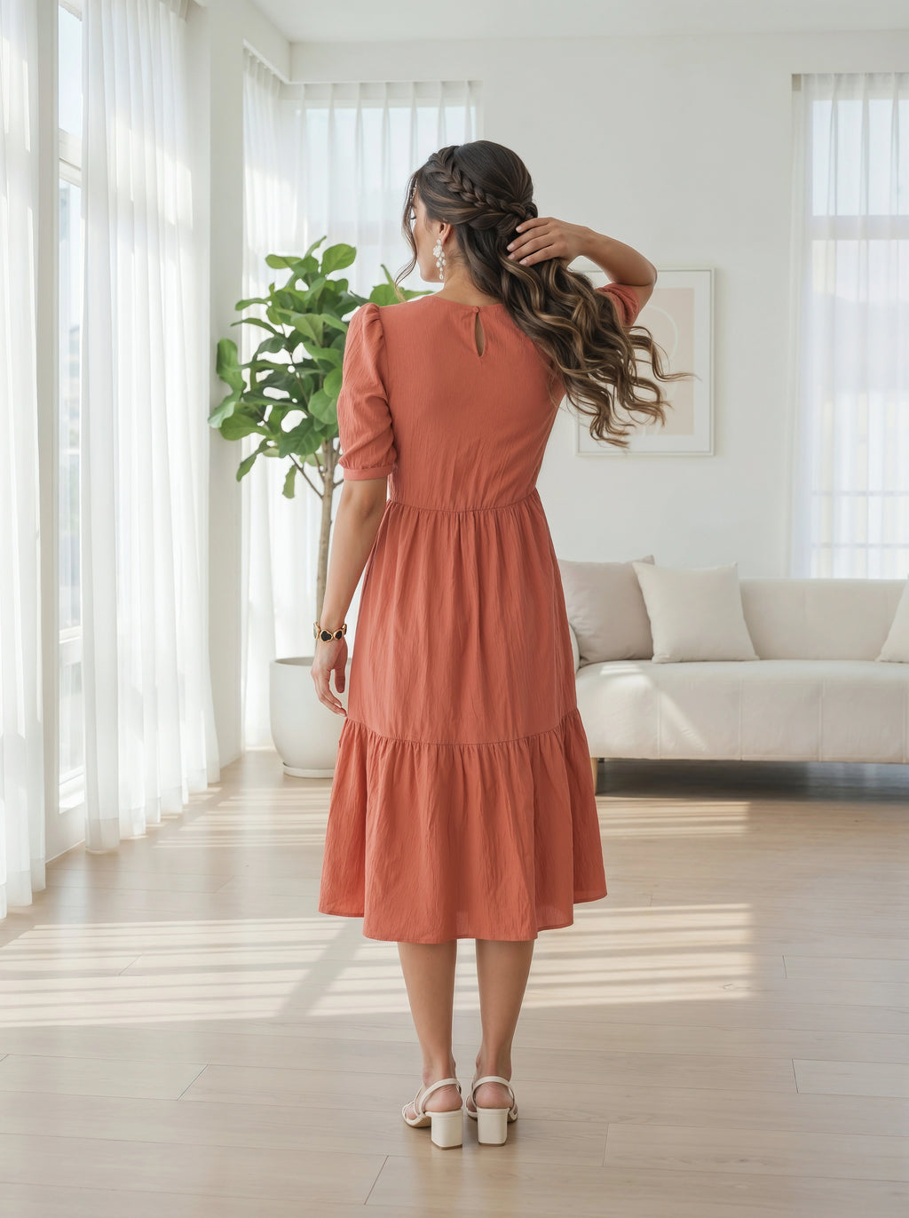 Woman in a rust-colored dress standing in a bright living room.