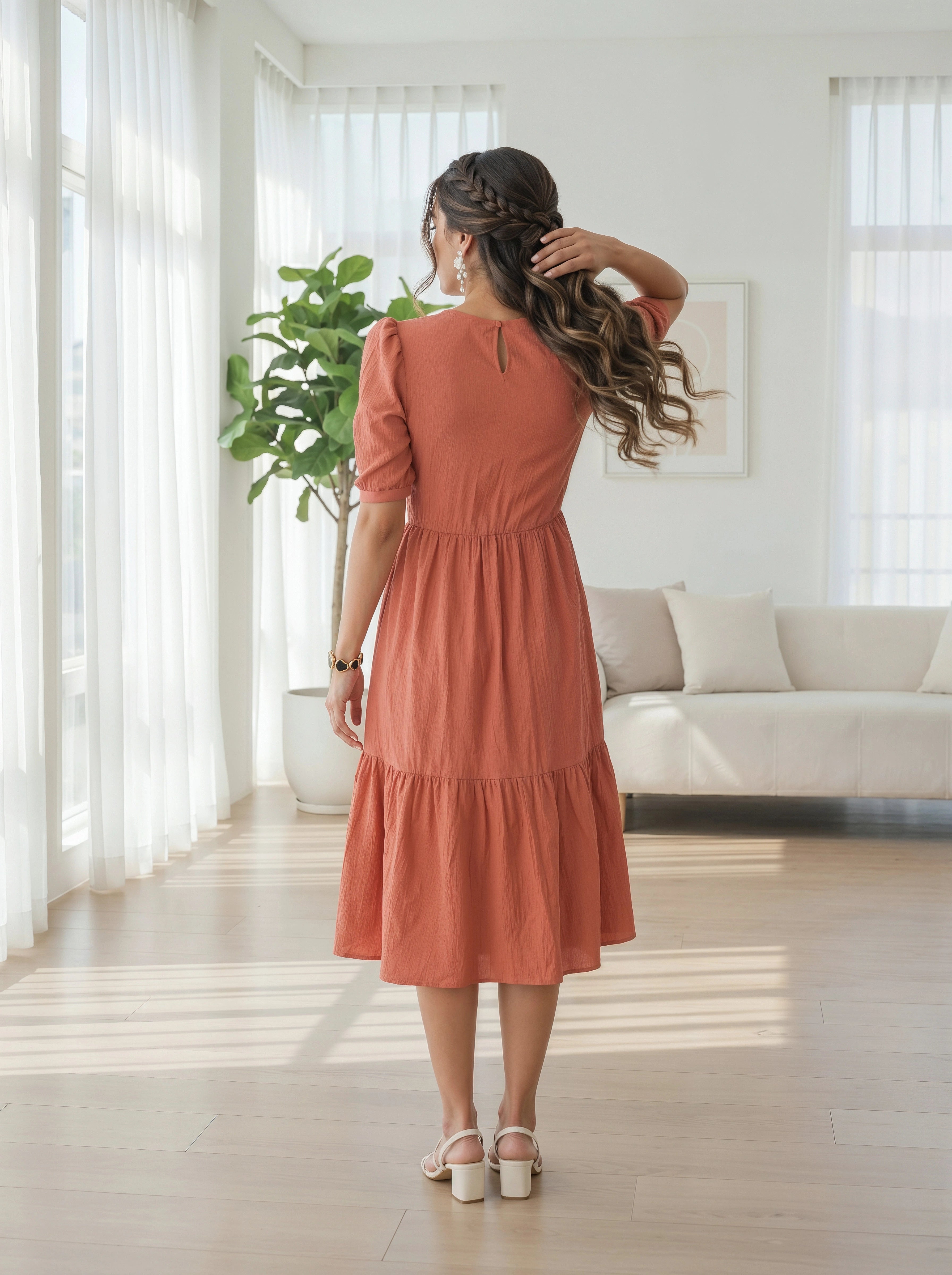 Woman in a rust-colored dress standing in a bright living room.