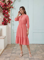 Woman in a pink dress standing in front of a floral decorated wall.