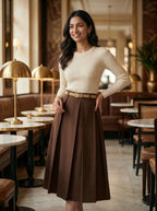 Woman in a beige sweater and brown skirt standing in a stylish cafe.