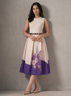 Woman wearing a cream dress with floral design and purple bottom half against a gray background