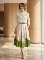 Woman wearing a white top and green skirt with floral design in an indoor setting.