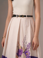 Person wearing a white sleeveless top and floral skirt with a plain background