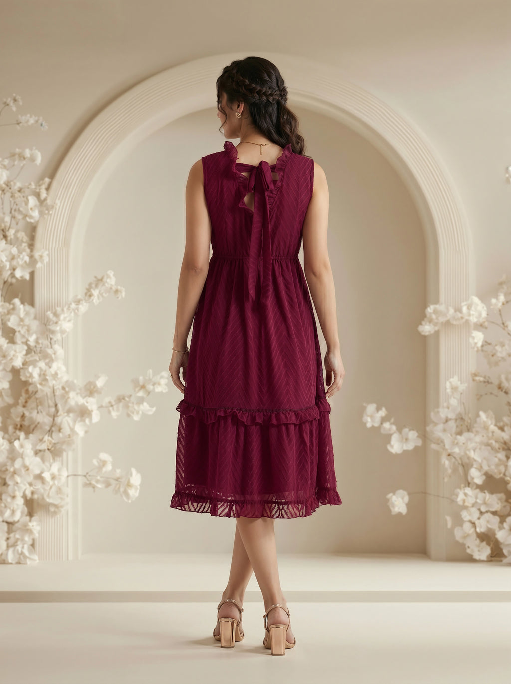 Woman wearing a burgundy dress with floral decorations in a softly lit room.