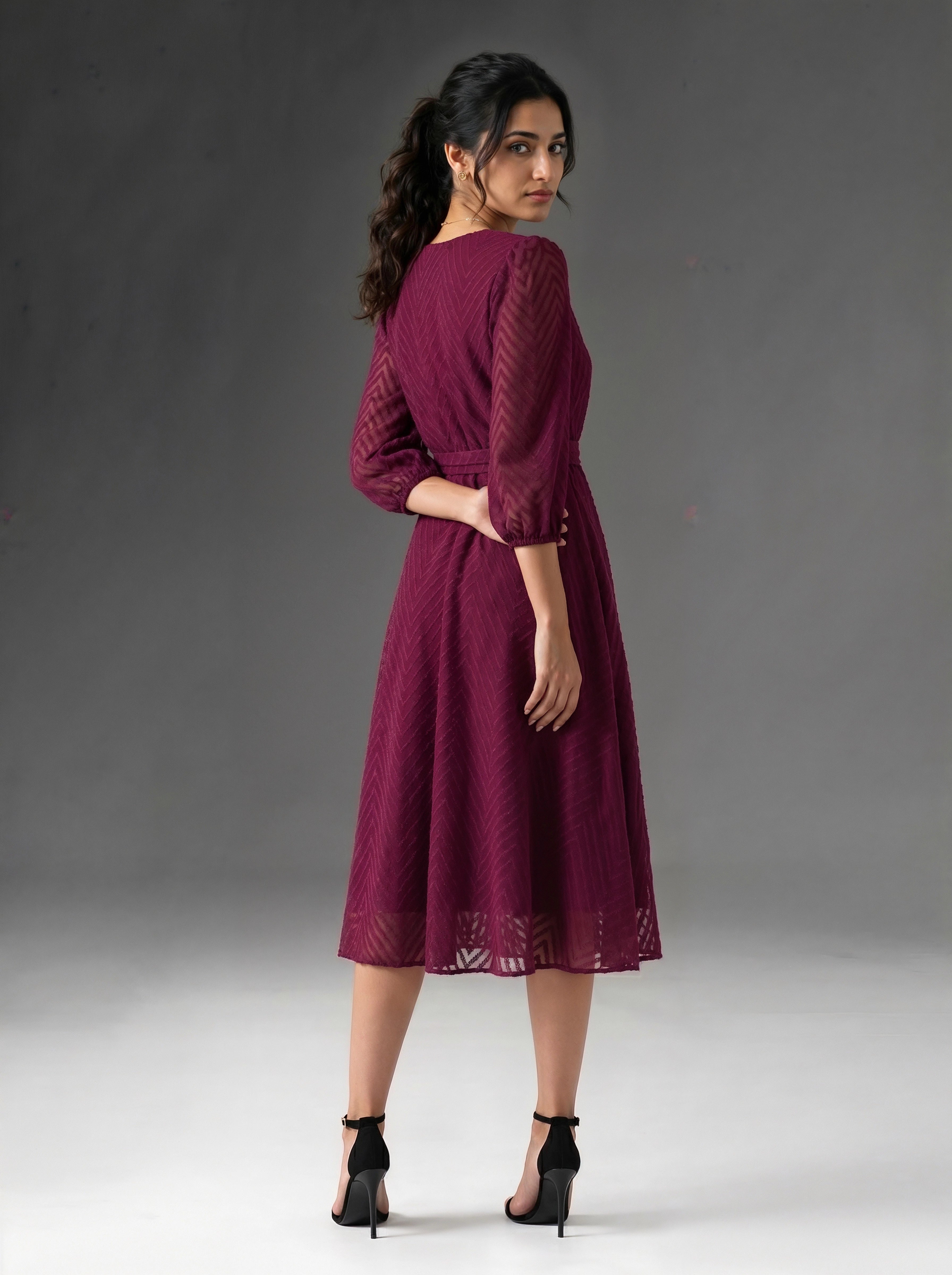 Woman wearing a burgundy dress with lace details on a gray background
