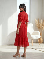 Woman wearing a navy blue dress standing against a beige wall with a plant.