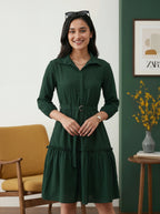 Woman wearing a green dress standing in a room with a yellow chair and decorative elements.