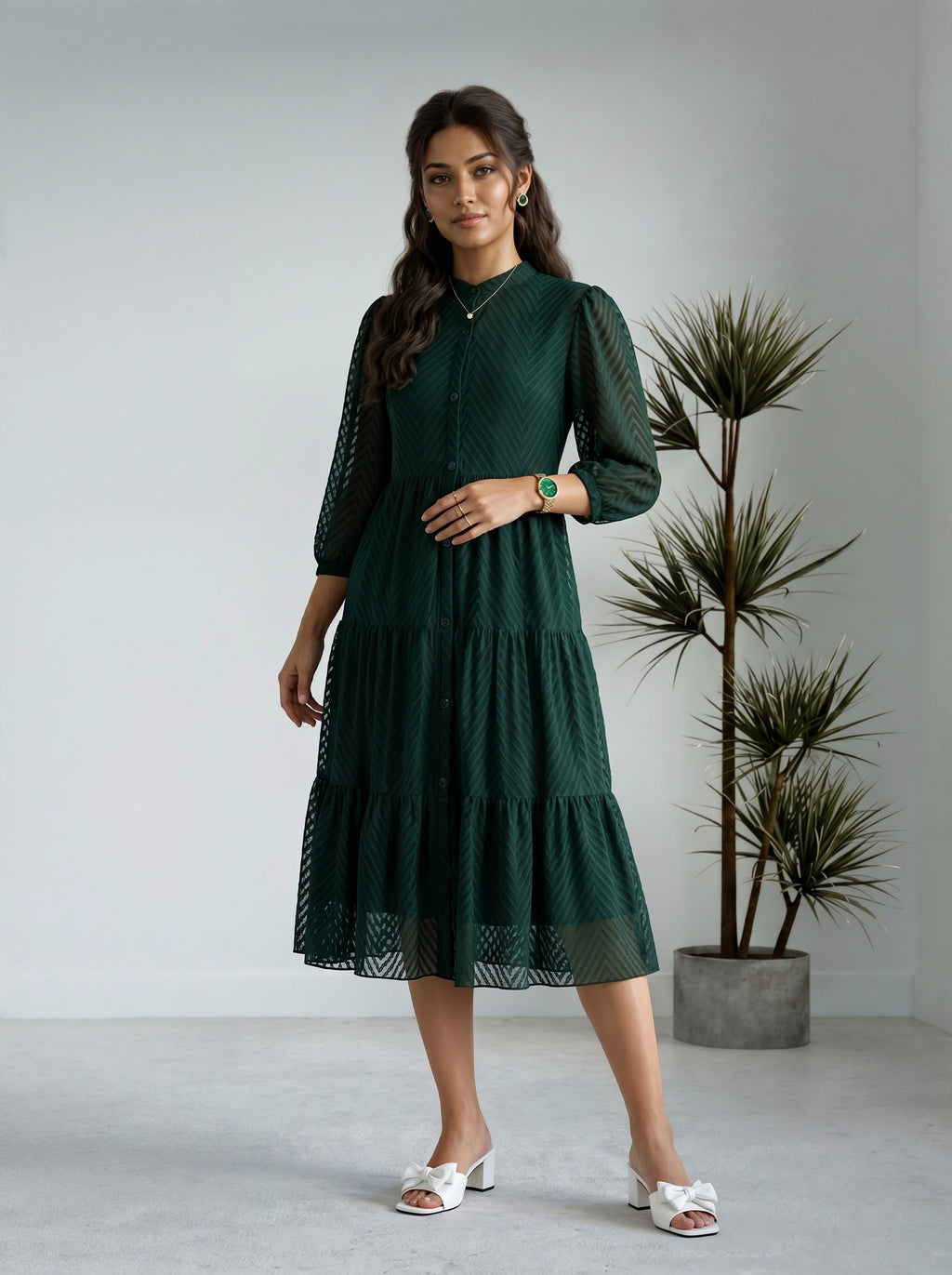 Woman wearing a green dress standing in a minimalistic room with a plant.
