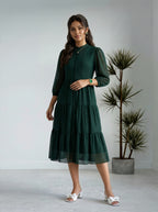 Woman wearing a green dress standing in a minimalistic room with a plant.