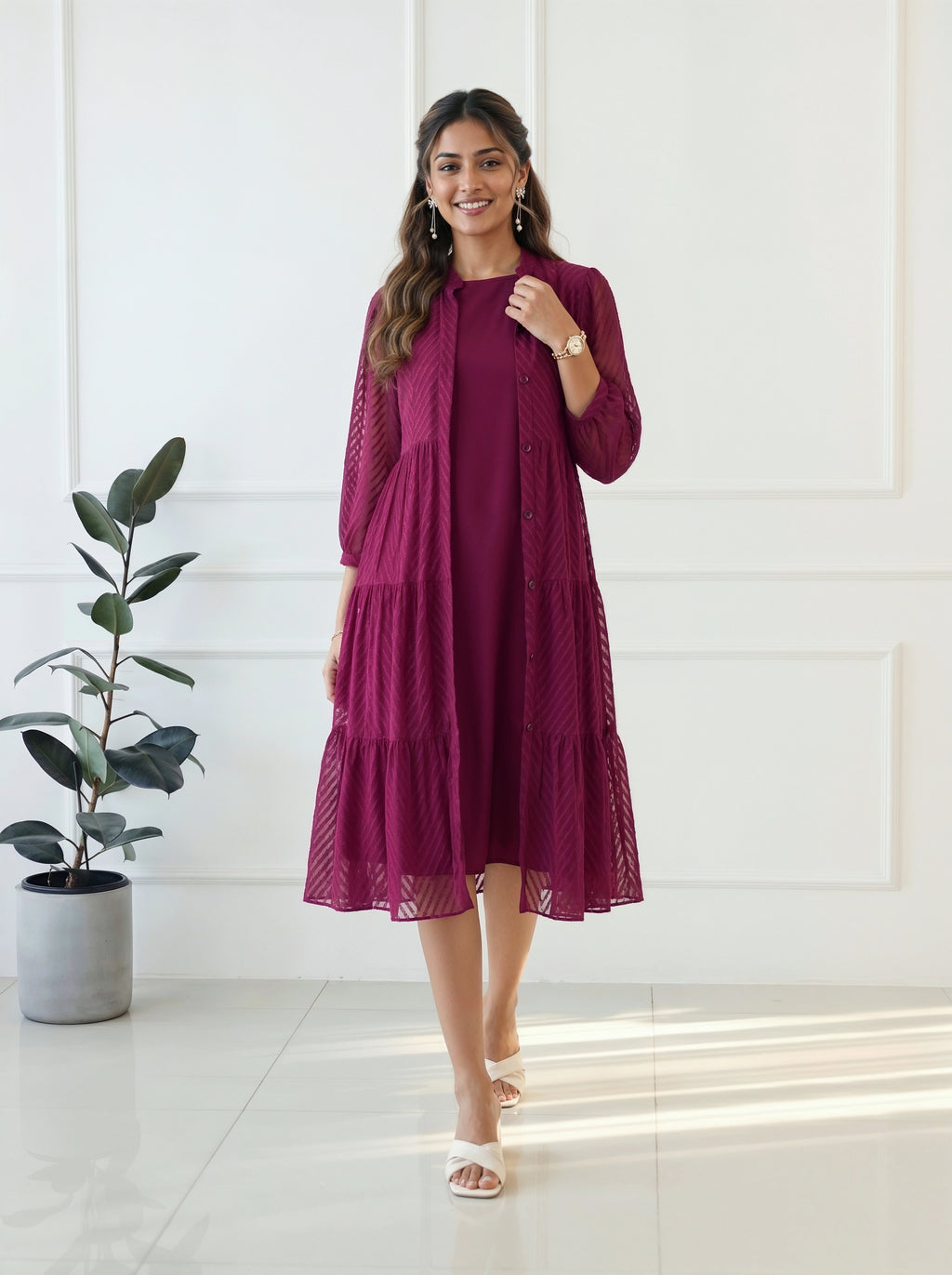 Woman wearing a burgundy dress standing in a bright room with a plant.