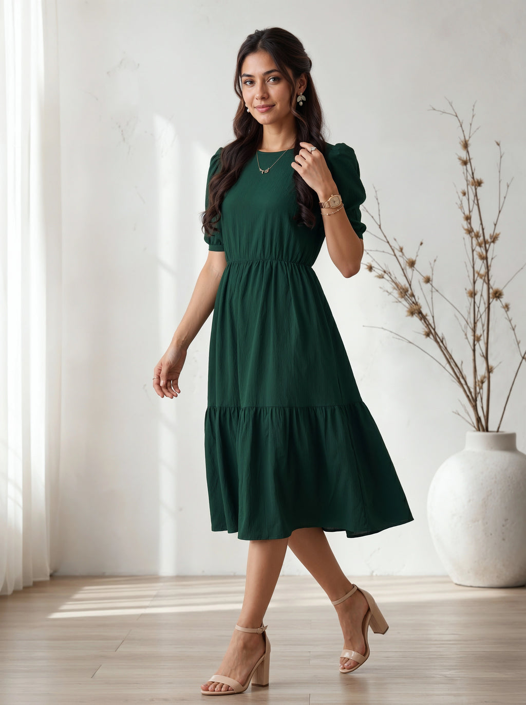 Woman wearing a green dress standing in a room with a white curtain and vase.