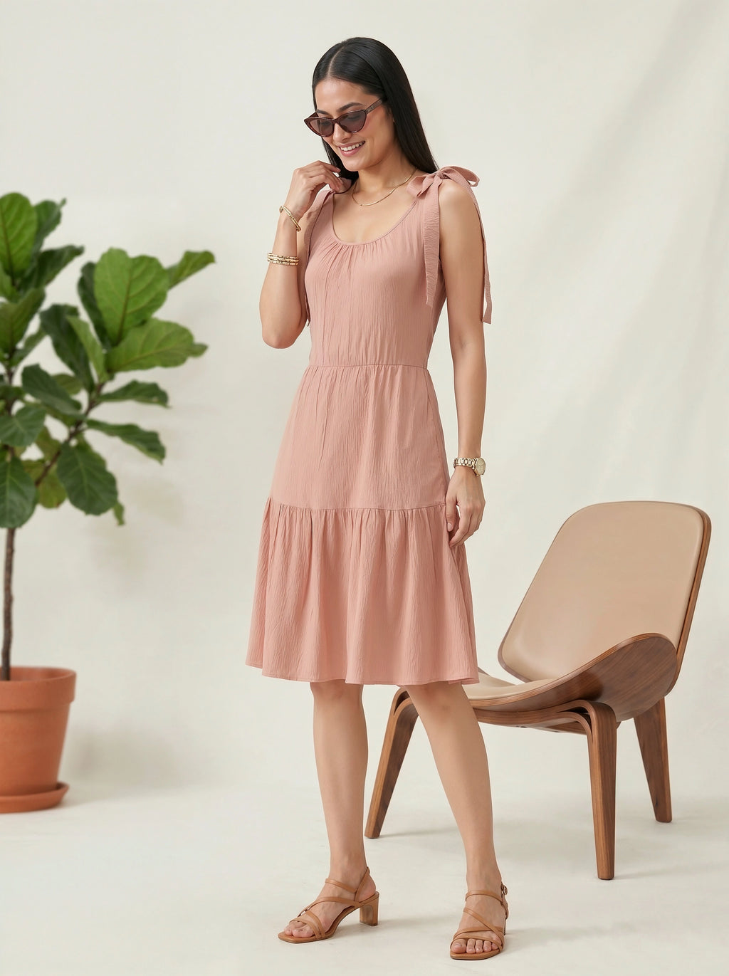 Woman in a pink dress standing next to a plant and chair on a light background