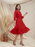 Woman in a red dress standing against a beige curtain with decorative plants.