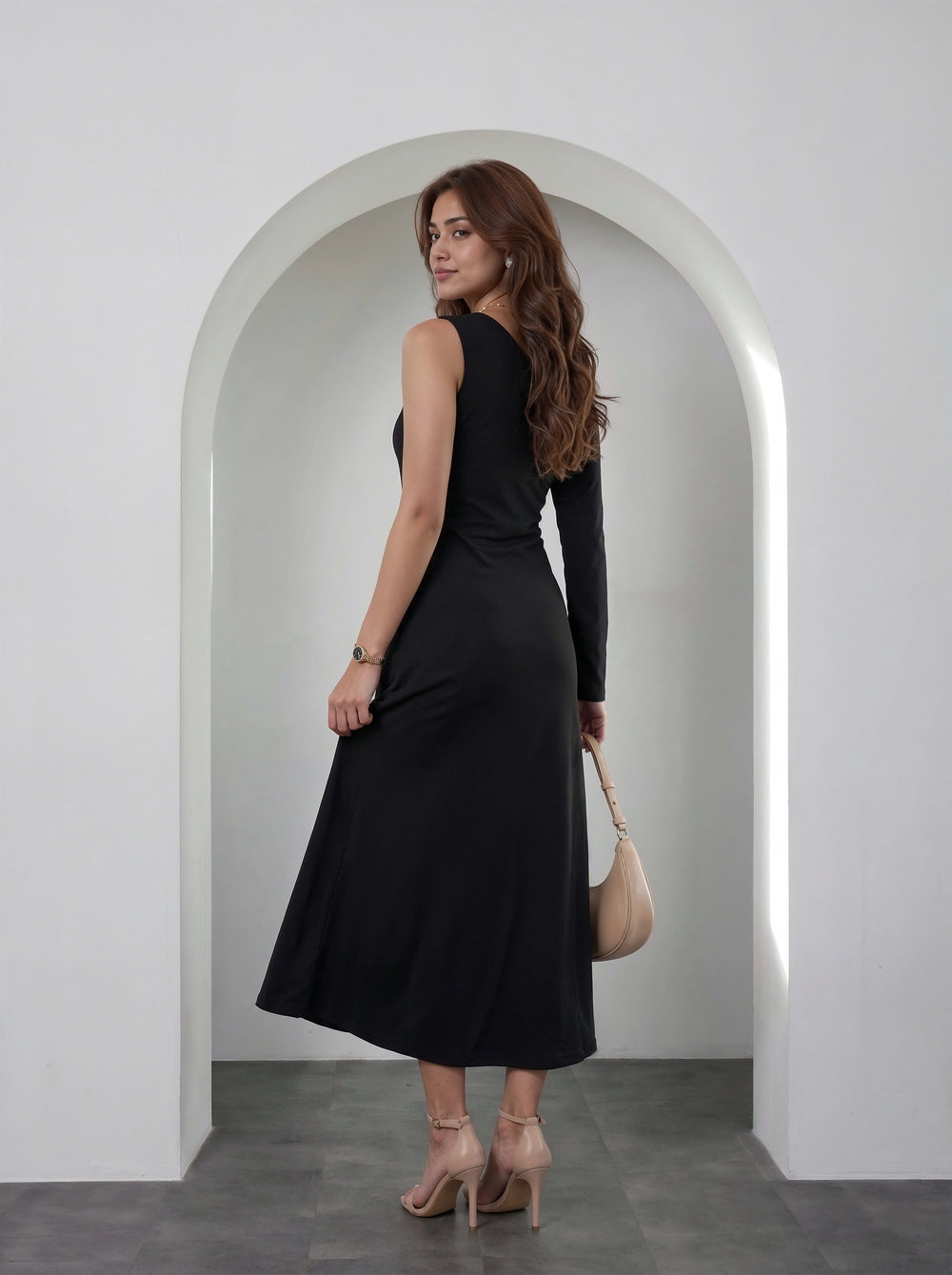 A woman wearing a sleeveless black midi dress with a long side slit, standing in front of a white arched doorway and holding a beige handbag.