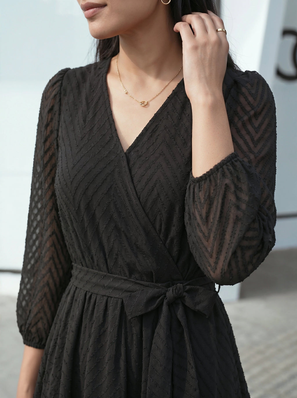 Woman wearing a black dress with sheer sleeves against a neutral background
