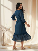 Woman wearing a blue dress standing in a softly lit room with curtains.