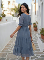 Woman in a blue dress walking on a stone path with white buildings and plants in the background
