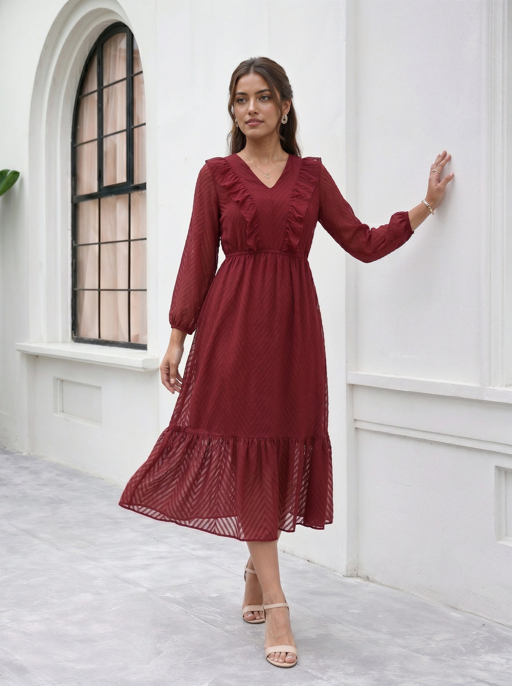 Woman wearing a red dress standing against a white wall with a window.