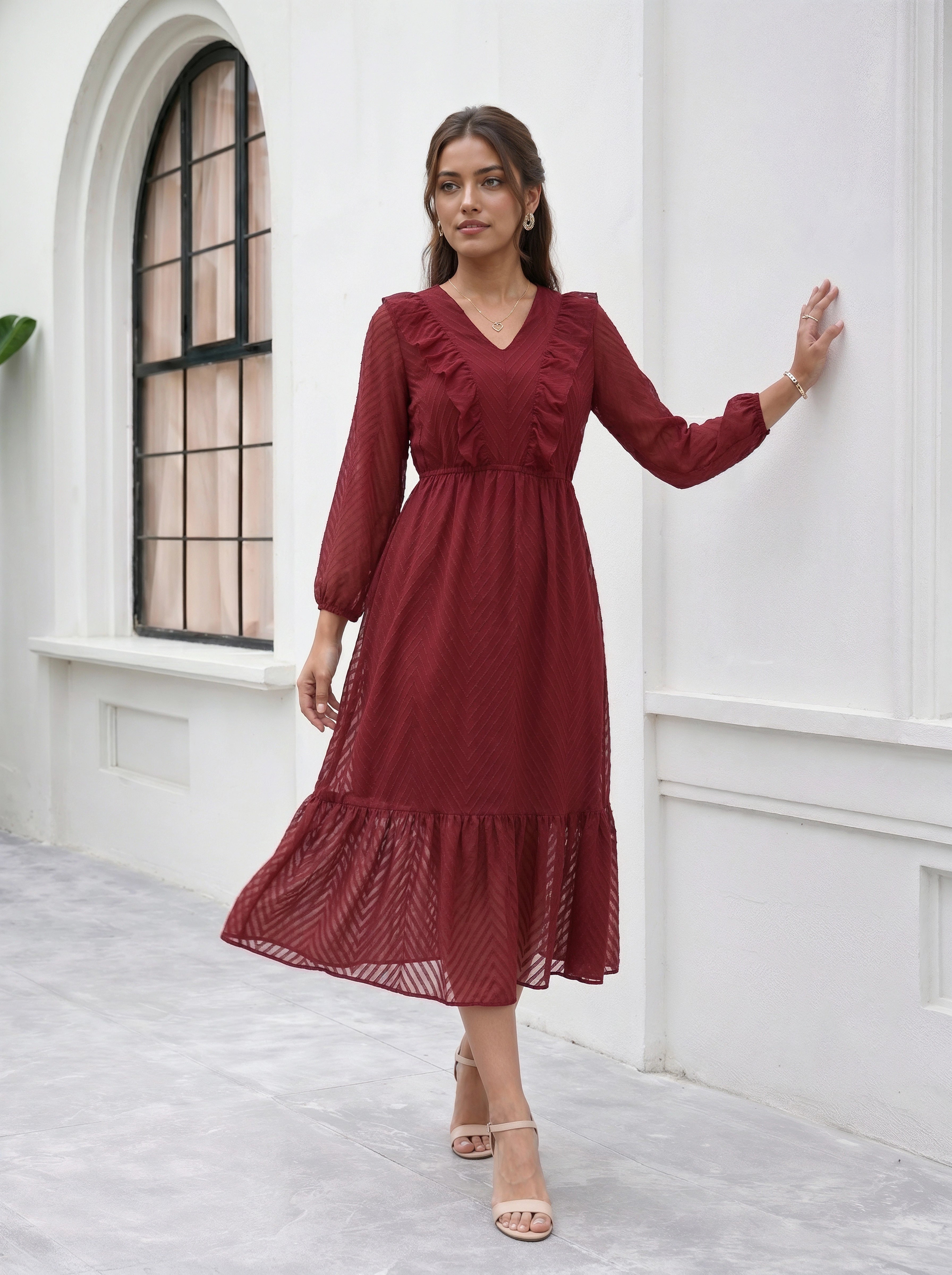 Woman wearing a red dress standing against a white wall with a window.