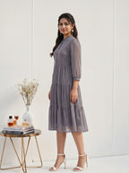 Woman in a gray dress standing next to a small table with a vase and books on a white background