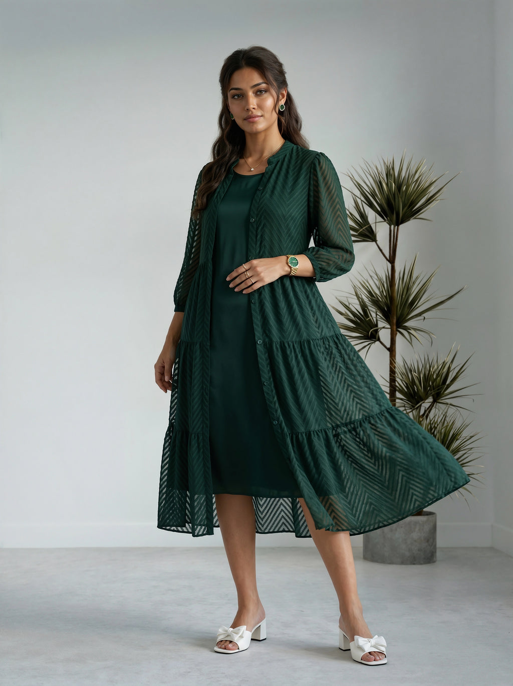 Woman wearing a dark green dress standing in a minimalistic room with a plant.