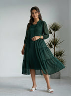 Woman wearing a dark green dress standing in a minimalistic room with a plant.