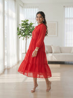 Woman in a red dress standing in a bright living room with white furniture and large windows.