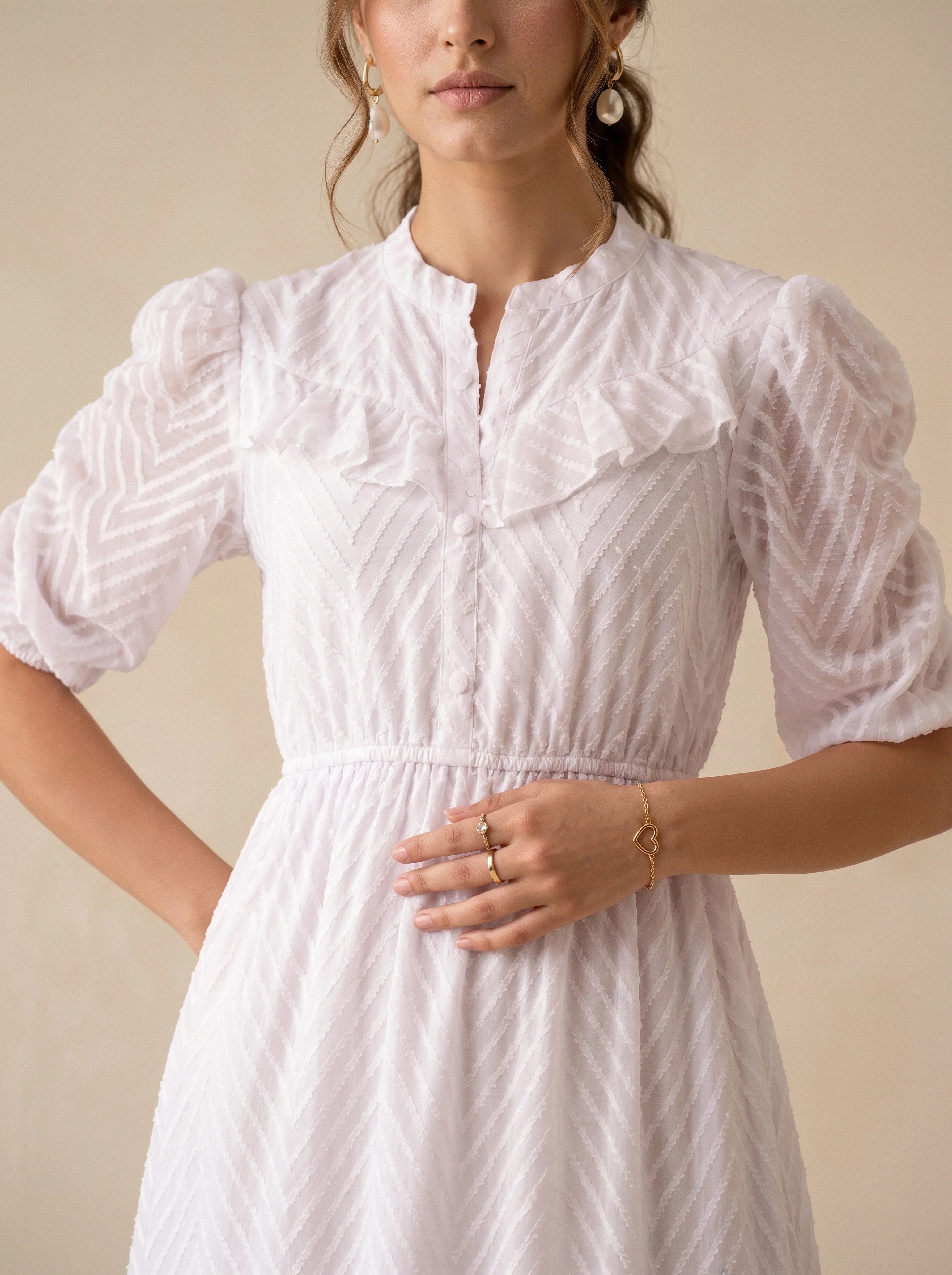 Woman wearing a white dress with ruffled sleeves against a neutral background
