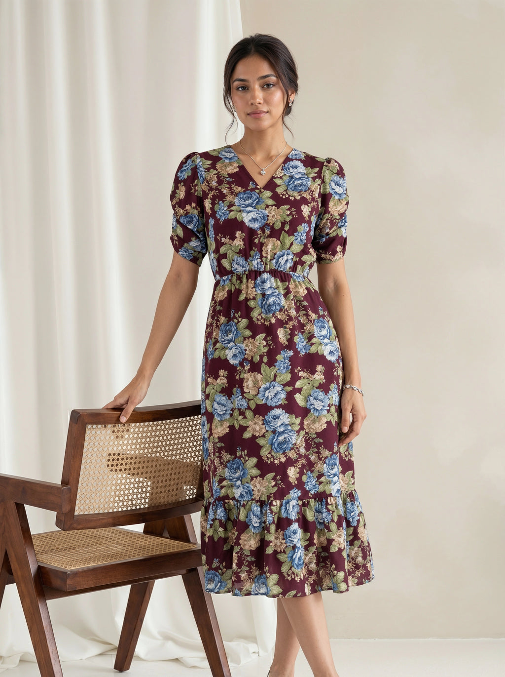 A woman modeling a dusty blue midi dress with a matching sheer open-front cardigan in a bright, sunlit white room with large windows.