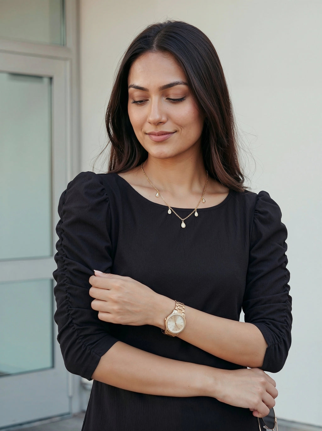 Woman wearing a black dress with puffed sleeves, gold watch, and jewelry.