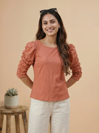 Woman wearing a rust-colored blouse with ruffled sleeves against a beige background