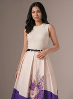 Woman wearing a white dress with floral design and purple bottom half on a plain background