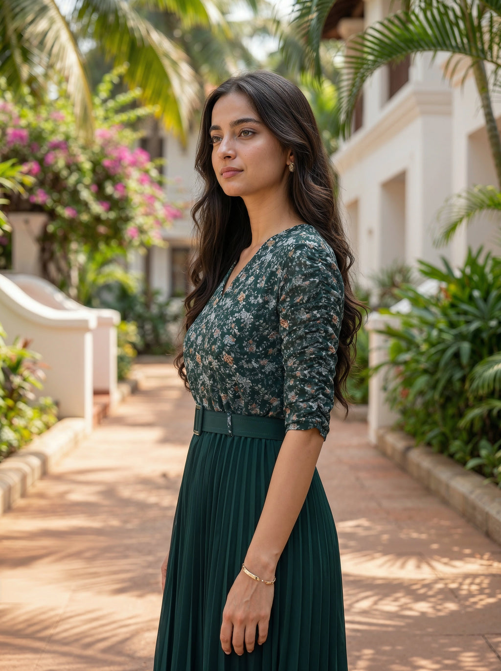 Woman in a green floral dress standing outdoors with plants and a building in the background
