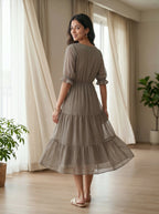 Woman wearing a gray dress standing in a room with curtains and plants.