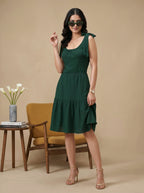 Woman wearing a green dress standing in a room with a chair and table.