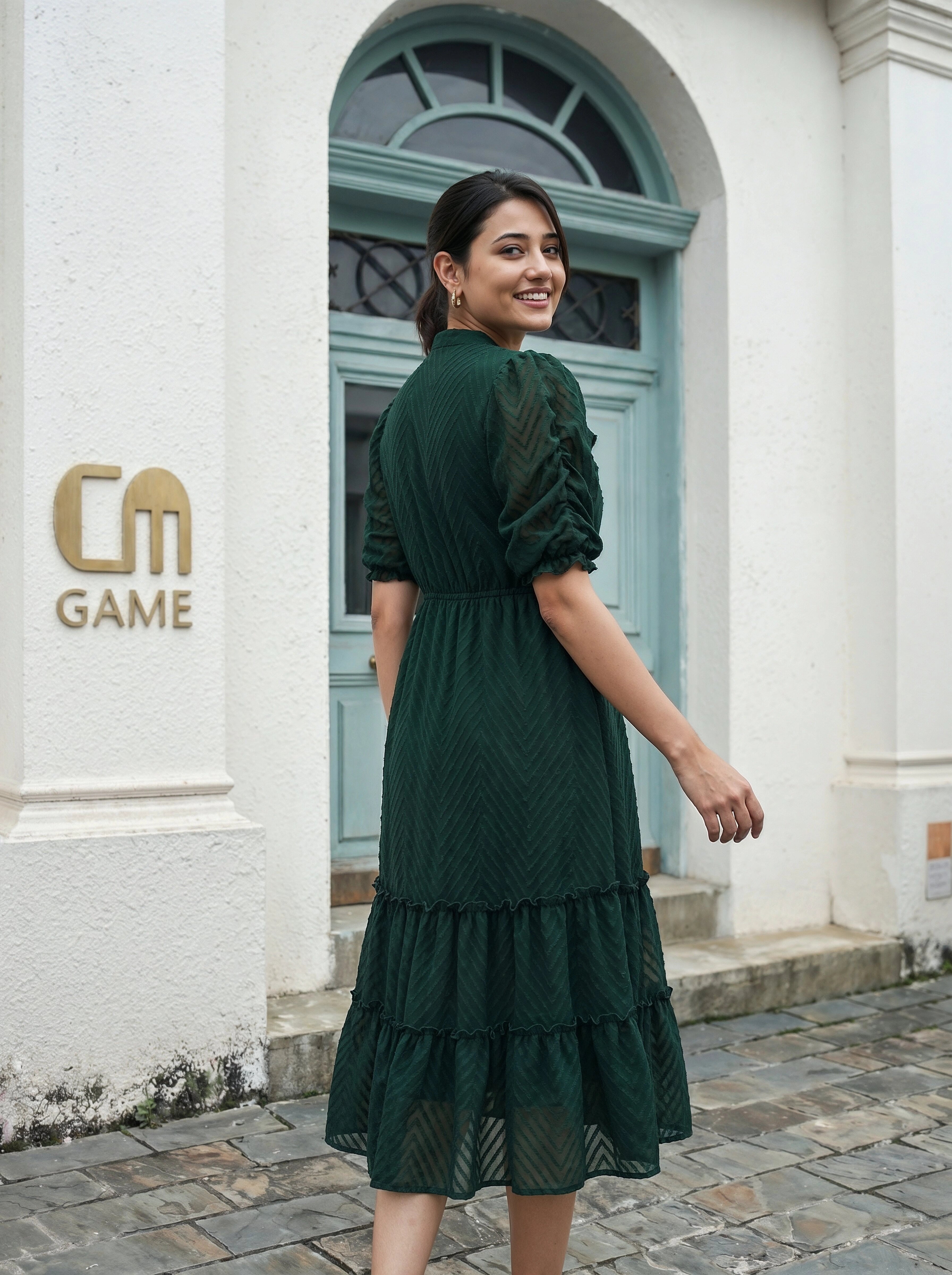 Woman in a green dress standing in front of a building with 'CM Game' logo.