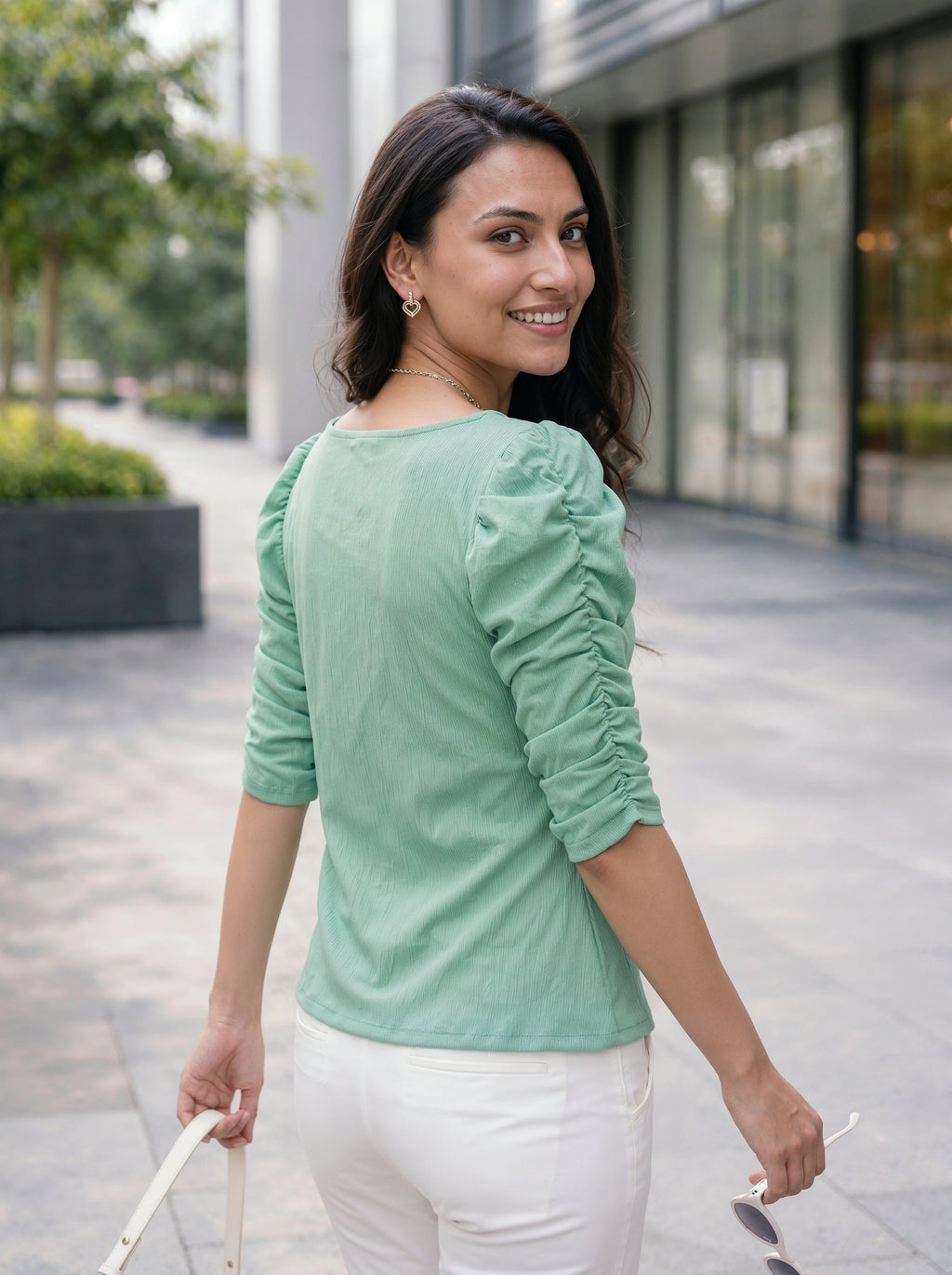 Woman wearing a light green top with ruched sleeves in an outdoor setting.