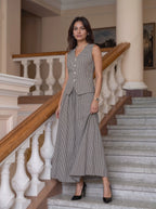 A woman models a sleeveless gray and white houndstooth vest and matching maxi skirt set on a grand staircase with white balustrades and wooden railings.