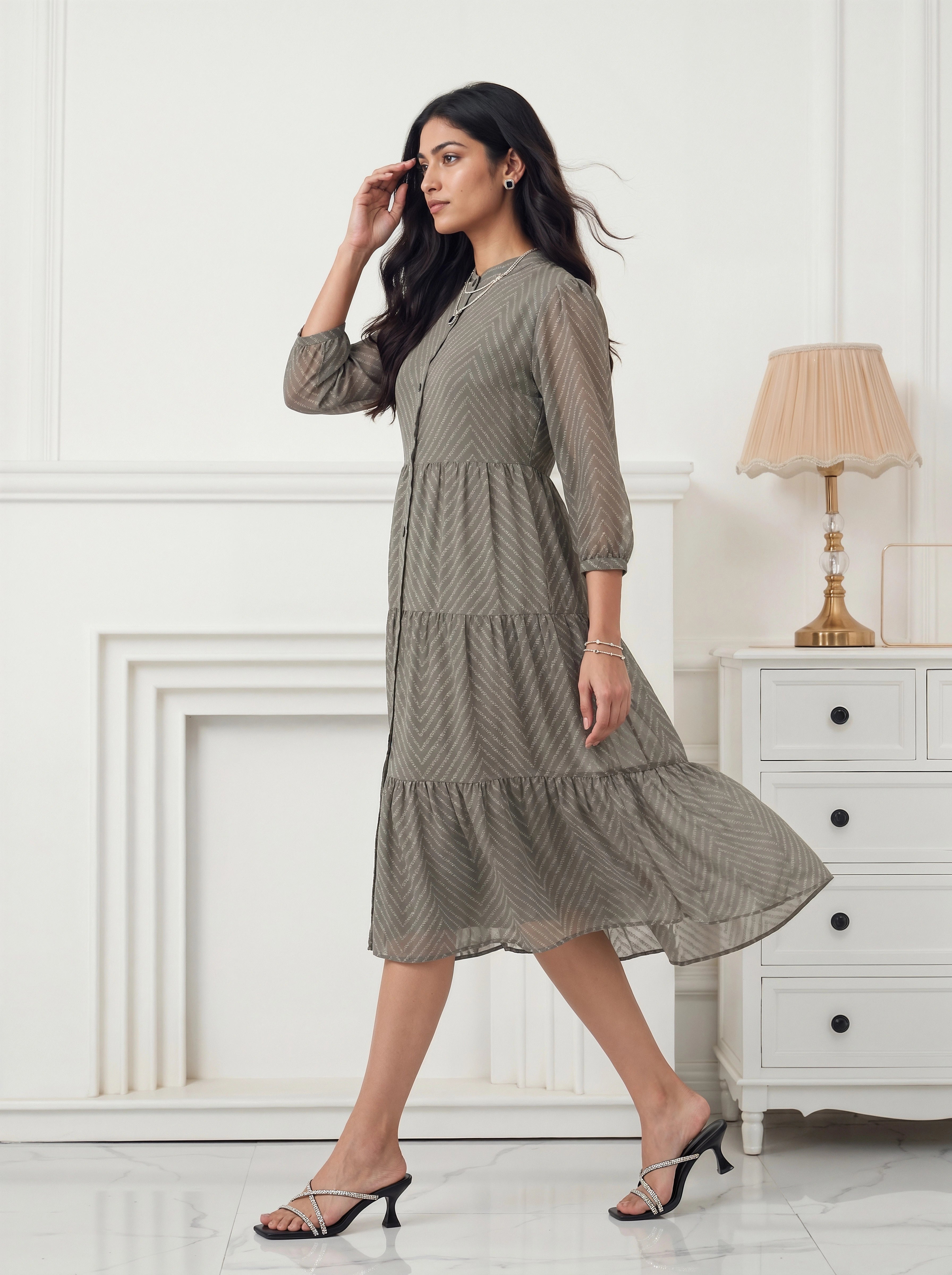 Woman wearing a patterned dress in a room with white walls and a lamp.