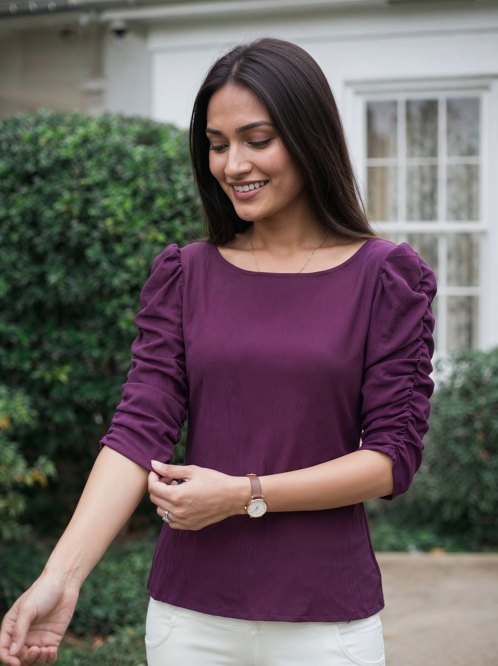 Woman wearing a purple top outdoors with greenery in the background