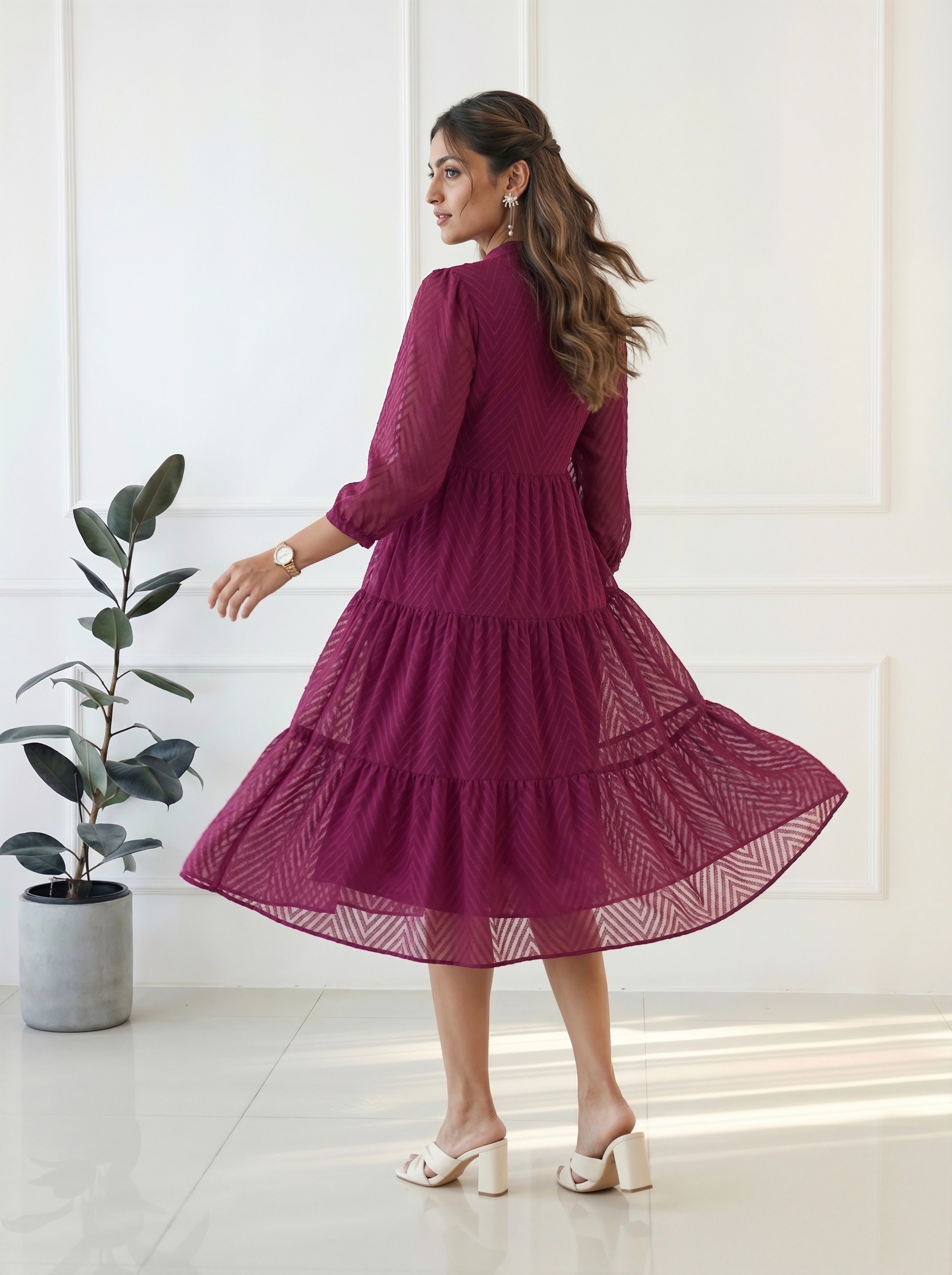 Woman in a burgundy dress standing in a room with a plant and white walls.