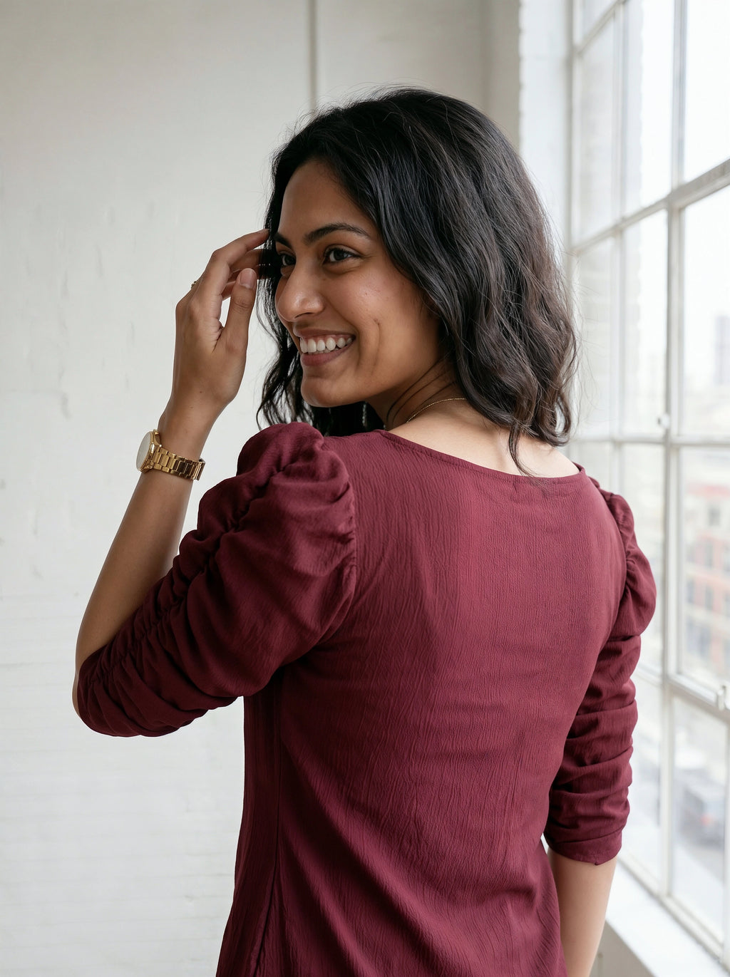 Woman wearing a burgundy dress with long sleeves, standing indoors near a window.