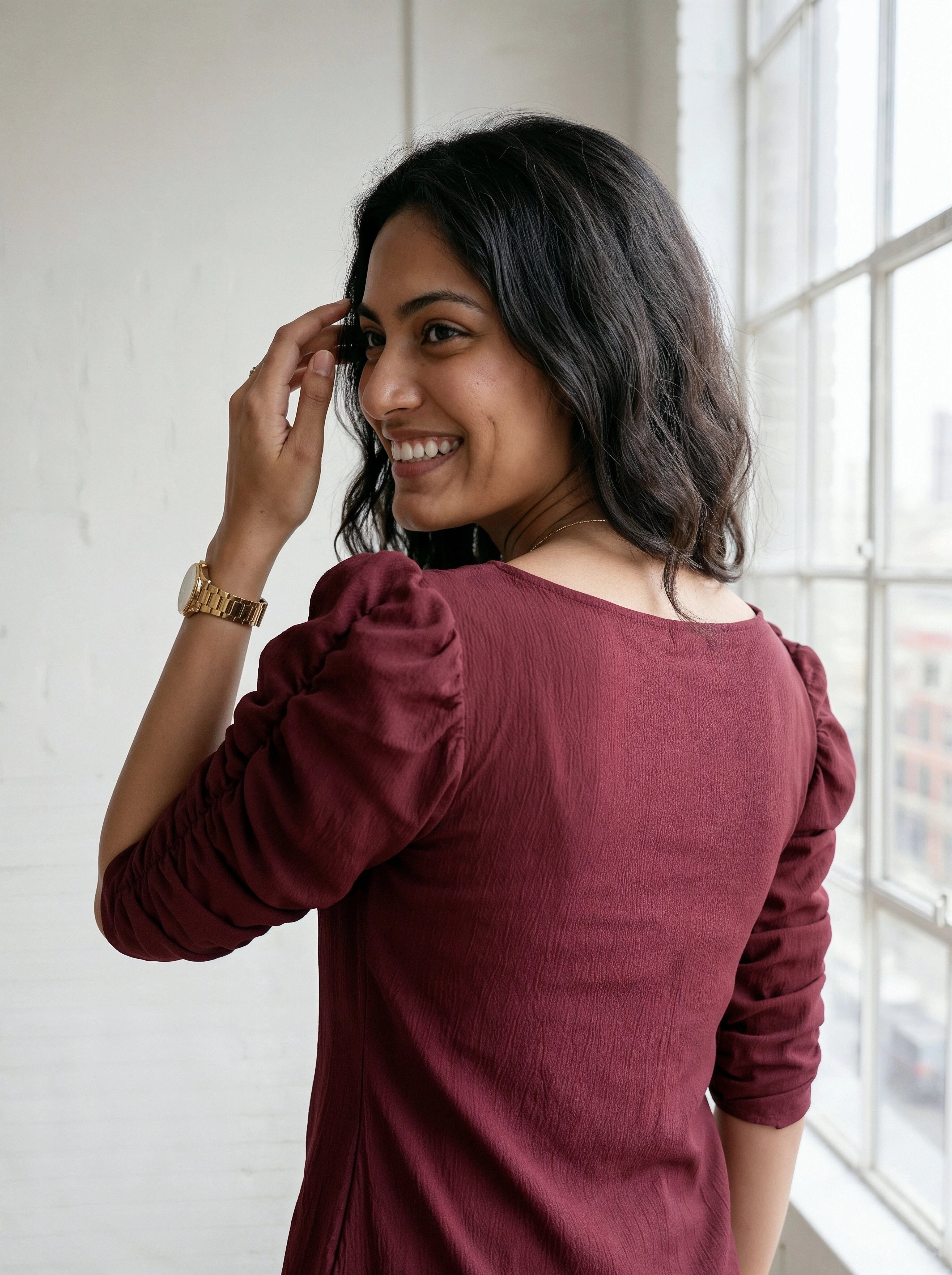 Woman wearing a burgundy dress with long sleeves, standing indoors near a window.