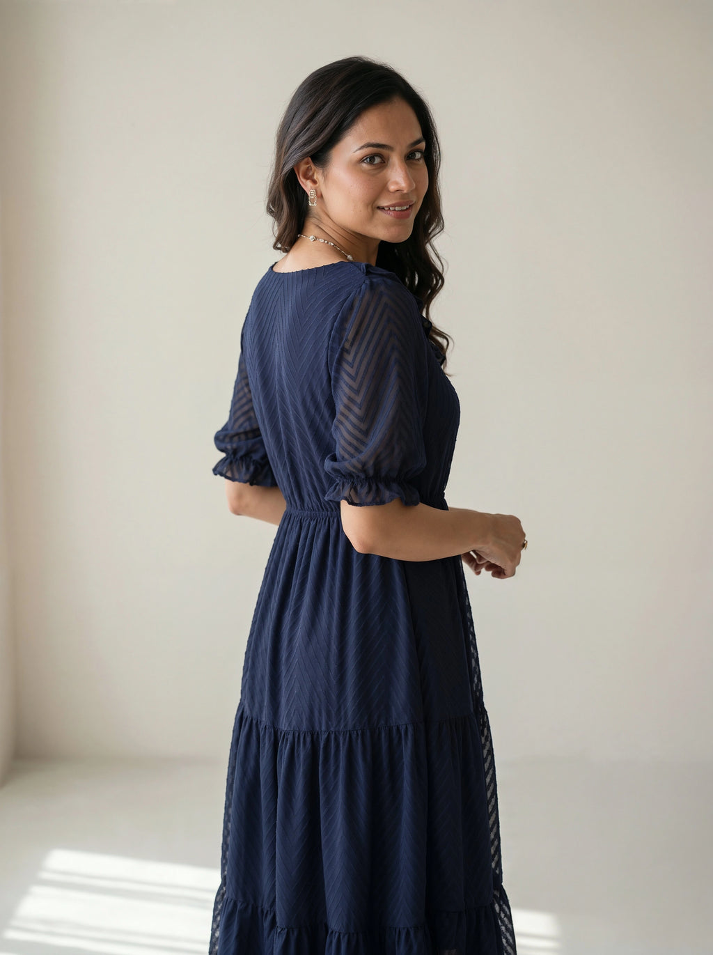 Woman wearing a navy blue dress with sheer sleeves against a plain background