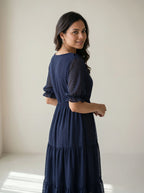 Woman wearing a navy blue dress with sheer sleeves against a plain background