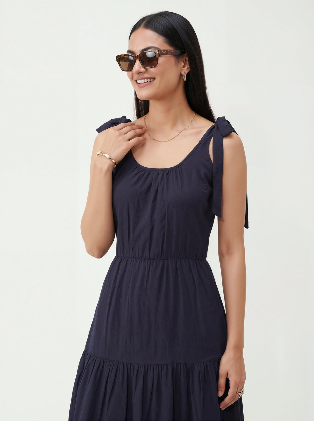 Woman wearing a navy blue dress with bow straps on a white background