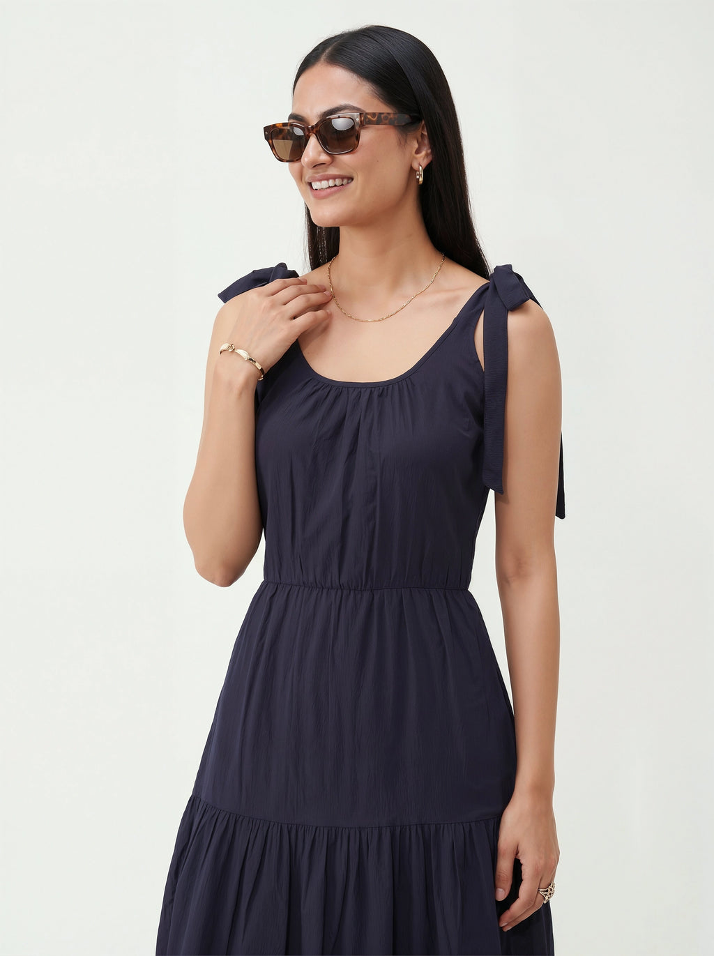 Woman wearing a navy blue dress with bow straps on a white background