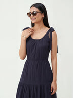 Woman wearing a navy blue dress with bow straps on a white background
