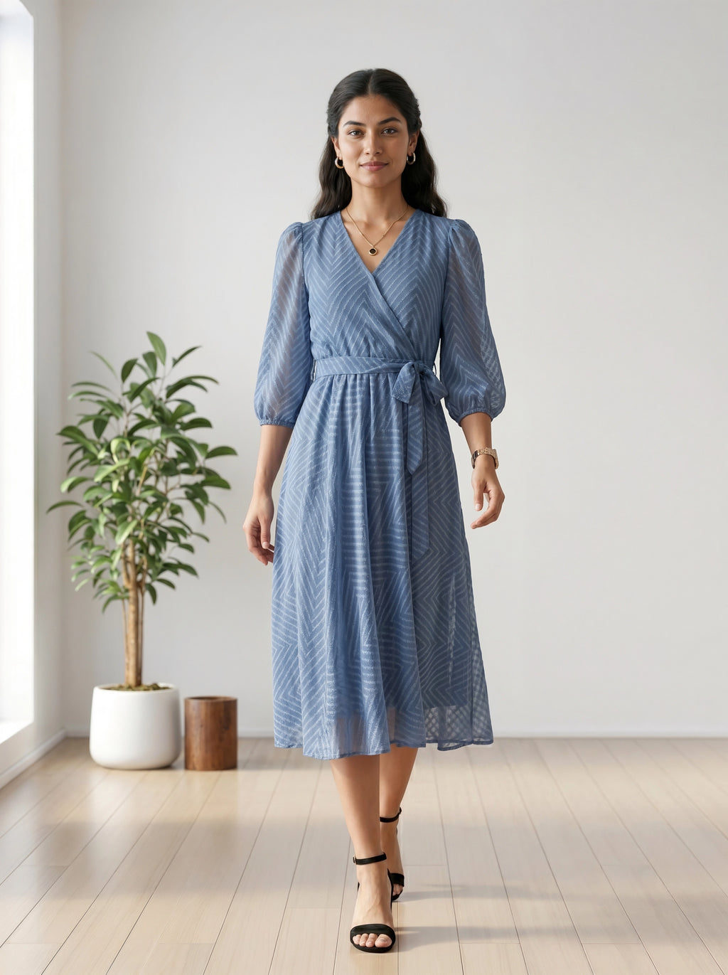 Woman wearing a blue dress standing in a room with a plant and wooden stool.